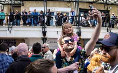 dad taking selfie in crowd with child on shoulders