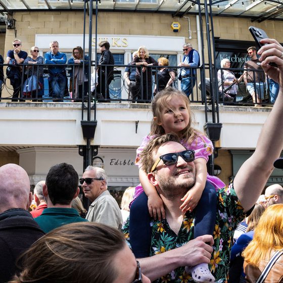 dad taking selfie in crowd with child on shoulders