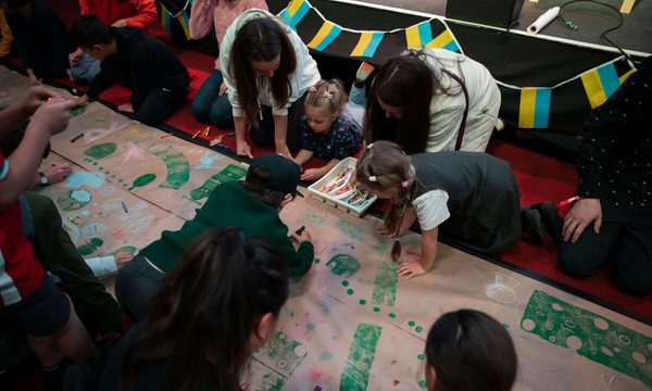 Children crowded around doing artwork. Ukrainian flag bunting hangs in the background.