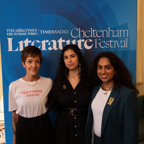 Three women posing in front of Cheltenham Lit Fest banner