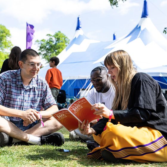 Three people reading this Jazz Festival brochure sat on the grass