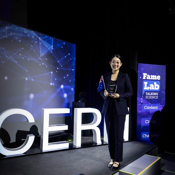 Tammy Lee, FameLab International Winner 2025 stood on the stage with her trophy in front of a sign that says CERN