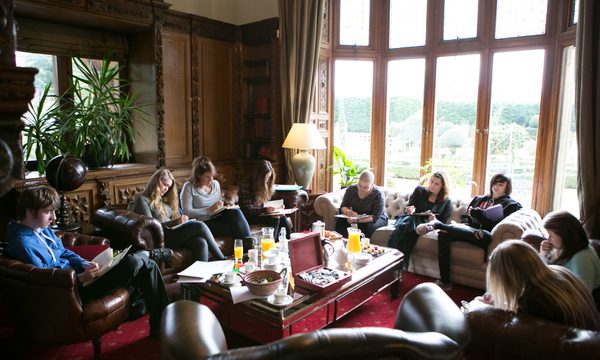 A group sit around a table in a large room writing