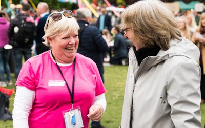 A woman wearing a pink t-shirt talking to a Festival-goer. She is smiling.