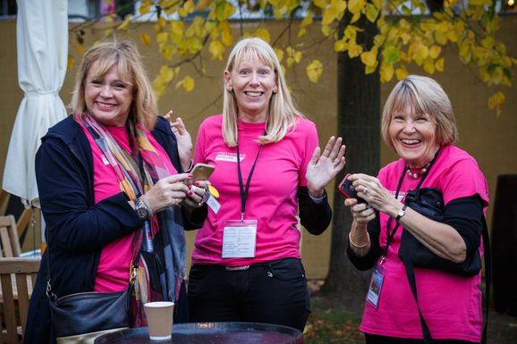 A group of three female volunteers wearing pink Cheltenham Festivals t-shirts. They are looking at the camera and smiling.