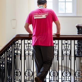 A Cheltenham Festivals volunteer stood at the top of the Town Hall stairs. He is wearing a pink Festival t-shirt.