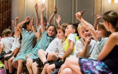 Primary school children sat in the front row of a concert with their hands in the air