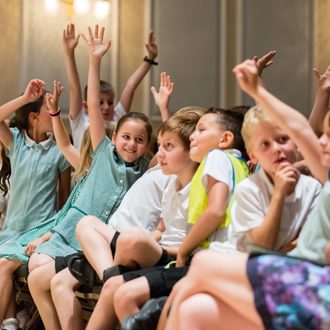 Primary school children sat in the front row of a concert with their hands in the air
