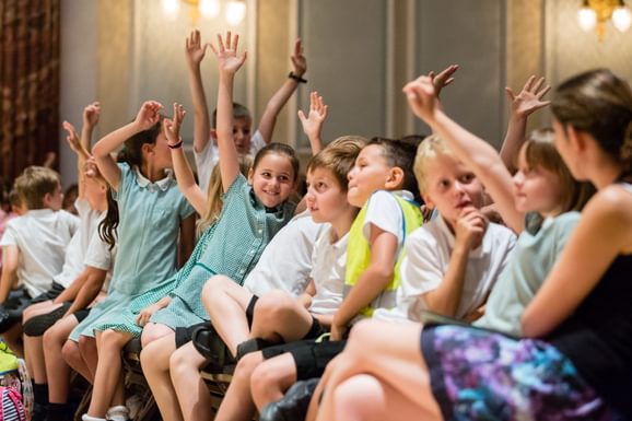 Primary school children sat in the front row of a concert with their hands in the air