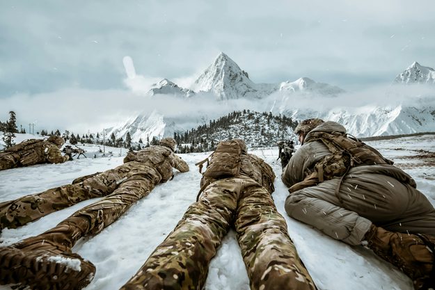 Three people in camo lie on the ground of the arctic