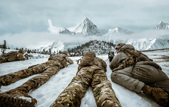 Three people in camo lie on the ground of the arctic