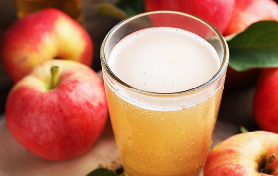 A glass of cider surrounded by apples