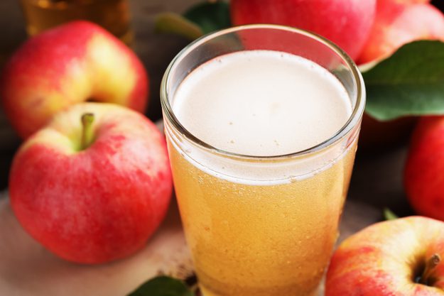 A glass of cider surrounded by apples