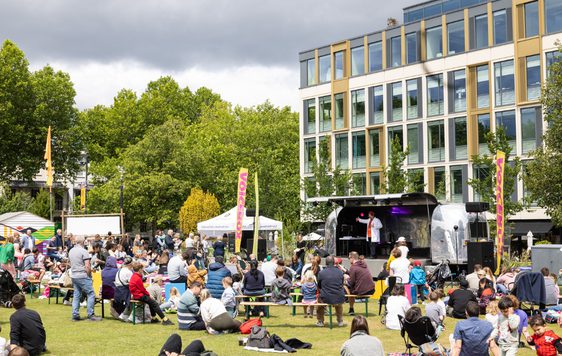 A busy Festival site with Festival-goers sat around the grass in front of the Jetstream venue