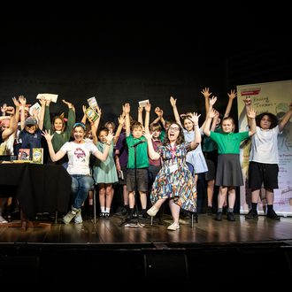 Children on stage cheering with their arms in the air at the RTRP Pupil Sharing Day