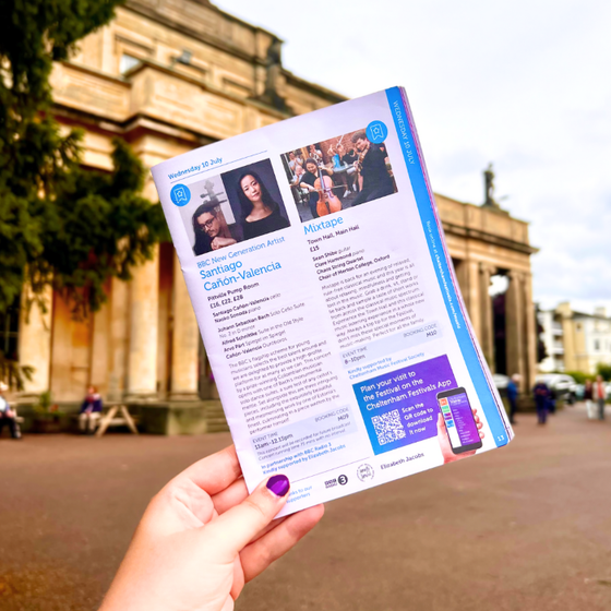 A hand holding a copy of the Cheltenham Music Festival brochure in front of Pittville Pump Rooms