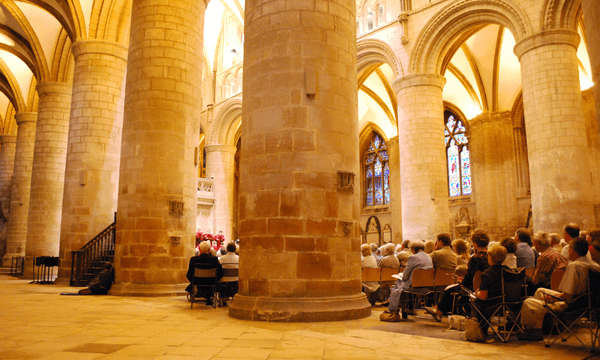 The interior of Gloucester Cathedral filled with a seated audience.