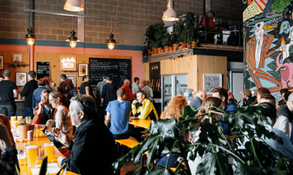 The busy Deya taproom. People sat talking on long benches surrounded by plants and quirky artwork.